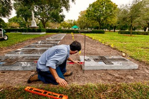 Nam Van Nguyen checks one of the refurbished memorials at the priests' burial section to ensure that is it properly aligned with one of the adjacent markers at the section south of the main outdoor altar at Calvary Catholic Cemetery.