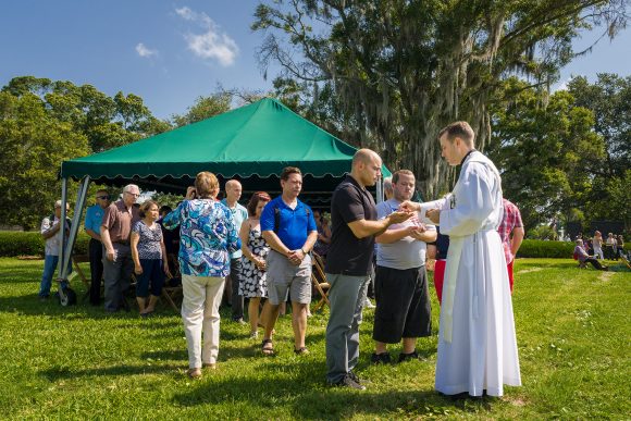 Msgr. David Toups distributes the Blessed Sacrament at Mass on Memorial Day at Calvary Catholic Cemetery, Clearwater, Fla.