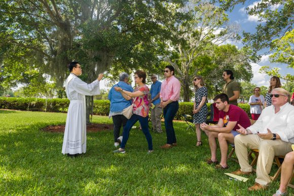 In the shade of a stately oak tree, the faithful receive Communion from Father Viet Nguyen at Mass on Memorial Day at Calvary Catholic Cemetery, Clearwater, Fla.