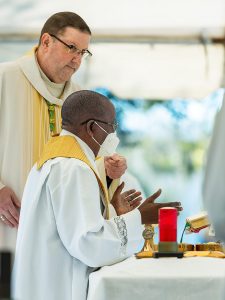 Father Hugh Chikawe, Chaplain at Calvary Catholic Cemetery, prays a portion of the Eucharistic Prayer as Bishop Parkes holds the microphone.