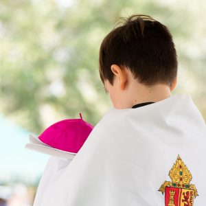 An altar server holds the bishop's mitre and zucchetto during Mass at Calvary Catholic Cemetery, Clearwater, Fla.