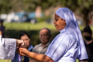 Sister Mary Dolores Urassa, CDNK receives the Eucharist during Mass at the outdoor altar on All Souls’ Day at Calvary Catholic Cemetery, Clearwater, FL.