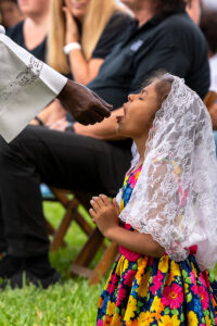A young communicant kneels as she receives the Eucharist at Mass on Memorial Day at Calvary Catholic Cemetery.