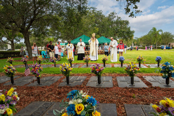 Bishop Parkes blesses the graves of priests who are buried adjacent to the altar after Mass on Memorial Day at Calvary Catholic Cemetery. From left to right are Father Hugh Chikawe, Father Ralph D’Elia, Bishop Parkes and Msgr. Robert Morris, VG.
