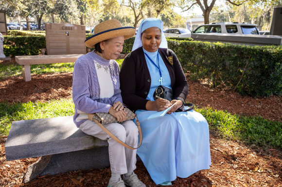 Yen Nguyen looks on as Sr. Mary Dolores Urassa, CDNK, prepares a note after Mass on All Souls' Day at Calvary Catholic Cemetery. Both women are members of the Legion of Mary and Sr. Dolores is a Pastoral Assistant at St. John Vianney Parish in St. Pete Beach.