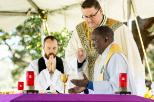 Fr. Hugh Chikawe, Chaplain of Calvary Catholic Cemetery, prays a part of the Eucharistic Prayer during Mass on All Souls' Day as Bishop Parkes holds the microphone for him.
