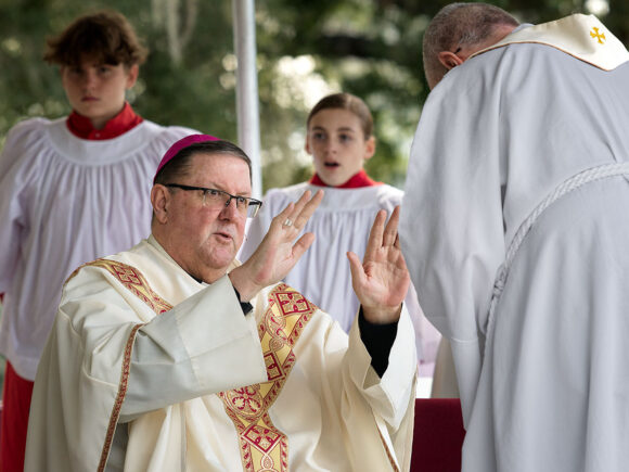 On the way to the ambo to proclaim the Gospel of John 6:37-40, Fr. Tom Morgan receives the blessing of Bishop Gregory L. Parkes.