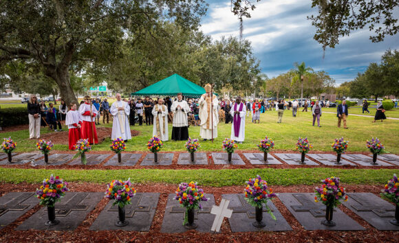 At the conclusion of the Mass, Bishop Parkes, concelebrating priests and the altar servers pause at the graves of some of the priests buried adjacent to the outdoor altar to pay their respects and pray. The priests, left to right, include Fr. Tom Morgan, Fr. Francis X. Buu, Fr. Ralph D’Elia, III, Bishop Parkes and Fr. Hugh Chikawe.